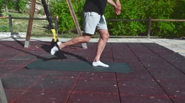 Spor kıyafetli bir adam açık hava eğitim alanında bacak egzersizi yapıyor, spor yapmaya ve aktif yaşam tarzına olan bağlılığını gösteriyor..