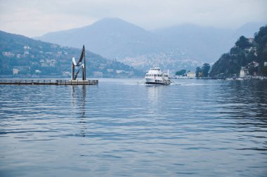 Sakin bir gölde gezinen bir teknenin huzurlu bir görüntüsü. Etrafı güzel tepeler ve evlerle çevrili. Sakin su, sakin ortamı yansıtır..