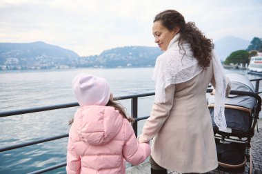 Bir anne ve kız göl kenarında huzurlu bir yürüyüş yapar, el ele tutuşur ve dağların ve suyun manzarasının tadını çıkarırlar..