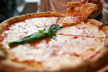 Yeni pişmiş pizzadan bir dilim sıcak, peynirli pizza kapan bir elin yakın çekimi. Yemek ve yemek temaları için mükemmel..