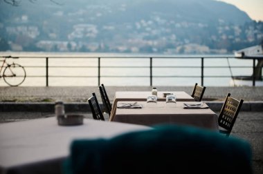 Boş masa ve sandalyeler dışarıda yemek için kurulmuş, sakin bir göle bakan sakin bir su ve manzaralı bir arka plan. Rahatlama, seyahat ve yemek kavramları için ideal..