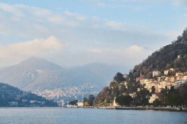 Como Gölü 'nün güzel manzarasında büyüleyici yamaçlı villalar ve bulutlu bir gökyüzünün altında sakin dağlar var. Seyahat ve doğa meraklıları için huzurlu ve resimli bir manzara..