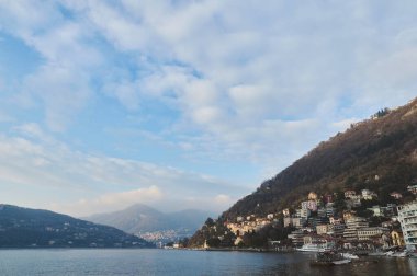 Tepeler üzerine evler inşa edilmiş güzel bir göl kenti. Sakin bir göle bakan, parlak mavi gökyüzü altında, tüylü bulutlar. Mükemmel seyahat yeri ve doğal manzara.
