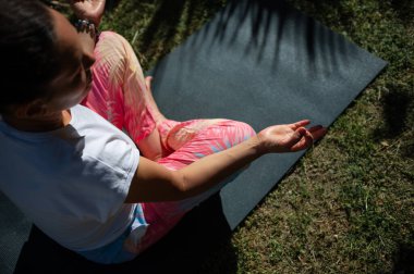 Bir kadın, yoga minderinde rahat bir şekilde meditasyon yapıyor. Doğal ortamdaki farkındalığı ve rahatlığı temsil ediyor..