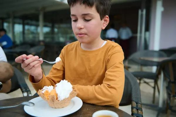 stock image Boy in a yellow shirt enjoying a scoop of ice cream in a waffle cone at an outdoor cafe, creating a moment of sweet delight.