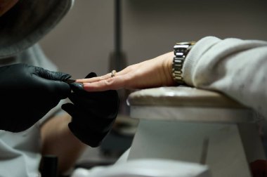 Güzellik salonundaki bir müşteriye manikür yapan bir manikürcünün yakın çekimi. Profesyonel, tırnaklarını şekillendirirken siyah eldiven giyiyor..