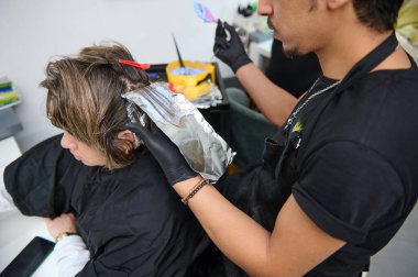 Bir kuaför, modern bir güzellik salonunda folyo tekniklerini kullanarak müşterinin saçına ustaca renk uygular..
