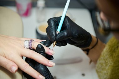 Profesyonel bir manikürcünün yakın plan çekimi. Güzellik salonuna tırnak cilası sürüyor. Kesin detaylara ve müşteri bakımına odaklanıyor..