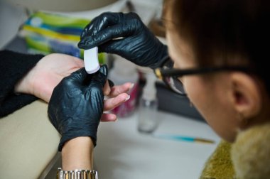 Eldiven giyen bir tırnak teknisyeni müşterinin tırnaklarını güzellik salonunda törpülüyor, profesyonel manikür bakımı sergiliyor..