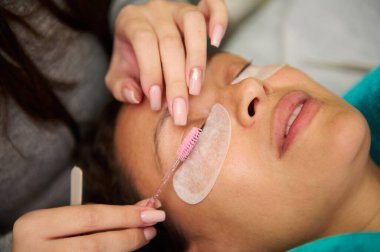 Güzellik salonunda kirpik uzatma tedavisi uygulayan bir kozmetikçi. Profesyonel kirpik tedavisi gören bir kadının yüzünü yakından çek..