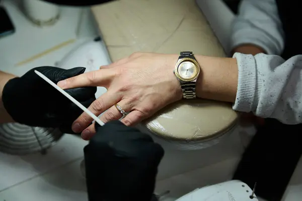 stock image Close-up of a professional manicure session at a beauty salon. A nail technician carefully files a client's nails, providing detailed nail care and attention.