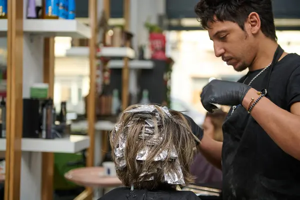 stock image A hairdresser applying highlights to a client's hair with foils in a well-equipped beauty salon. Professional service and expertise in hair care.
