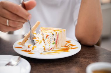 Beyaz bir tabakta krem şanti ve karamel serpiştirilmiş dondurmalı pastanın tadını çıkaran birinin yakın çekimi. Rahat ve hoşgörülü bir an..