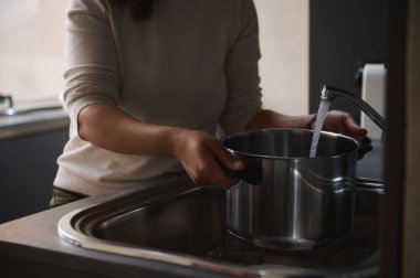 Mutfak lavabosunda bir tencereyi suyla dolduran, günlük ev işlerini yapan birinin yakın çekimi..
