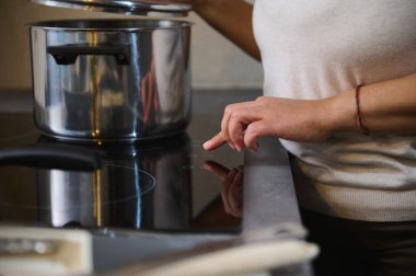 Modern bir mutfakta paslanmaz çelik tencereyle pişirmek için indüksiyon sobası kullanan biri. Sıcaklığı ayarlama ayarlarının yakınlaştırılması.