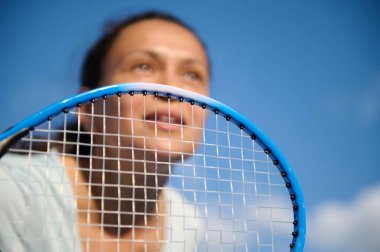 Bir bayan tenisçi kameraya yakın bir tenis raketi tutarken yoğun bir şekilde oyununa konsantre oluyor. Görüntü, bir kararlılık ve sportmenlik anını yakalar..