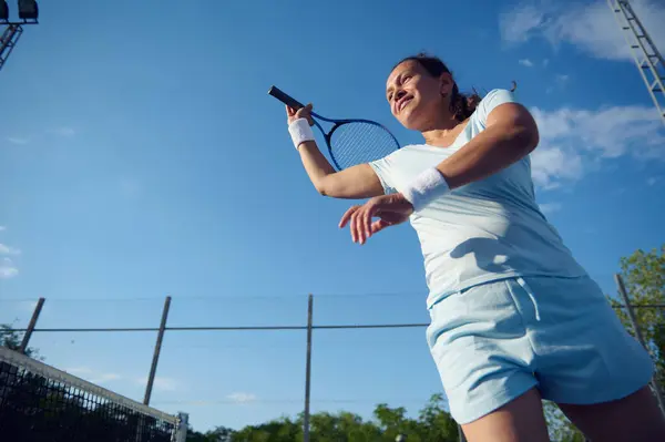 stock image A determined woman playing tennis on an outdoor court. She is mid-swing with a clear blue sky in the background.