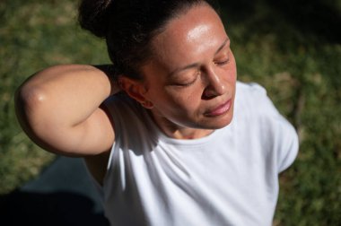 Kapalı gözlü ve rahat yüzlü bir kadın gün ışığında dışarıda meditasyon yapar. Doğal bir ortamda farkındalığı, rahatlığı ve huzuru sembolize eder..