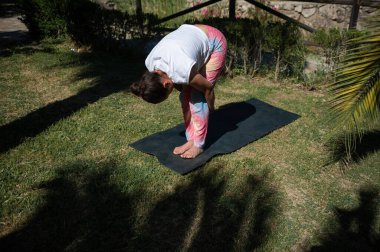 Kadın yoga yapıyor ve sakin bir bahçe ortamında paspasın üzerinde geriniyor. Doğayı ve refahı kucaklamak.