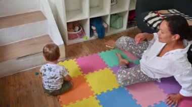 Evde rengarenk bir yapboz halıda anne ve bebek kaynaşıyor, renkli ekolojik olarak dost canlısı ahşap eğitim oyuncaklarıyla oynuyor. Bebek ahşap bir piramitle çarpışır.
