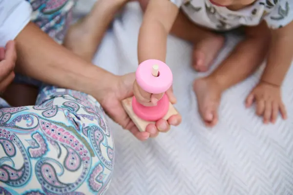 stock image Top view wooden pyramid in woman's hands, playing with her child educational games, stacking round circles, sitting together on linen blanket outdoors. Eco toys for kids development and entertainment