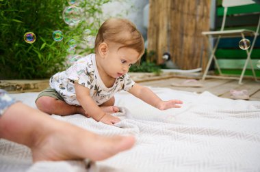 Bahçe bahçesinde sabun köpüğüyle oynayan tatlı bir erkek bebek. Kızıl saçlı beyaz çocuk baloncukları açık havada yakalıyor ve uçan baloncuklara ilgi gösteriyor. Çocuklar ve mutlu bir çocukluk. Eğitim ve öğrenim