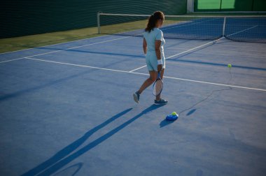Tenis antrenörüyle tek başına tenis oynayan bir kadın. Oyuna odaklanmış, güneşli günün tadını çıkarıyor..