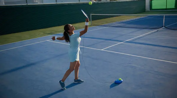 stock image A woman in sportswear practicing her tennis serve on an outdoor court using a ball machine. Perfecting her technique in preparation for an upcoming match on a sunny day.