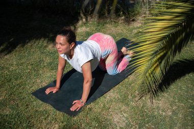 Açık havada yoga pozu veren bir kadın, güneşli havanın tadını çıkarıyor ve çevresi yeşilliklerle çevrili..