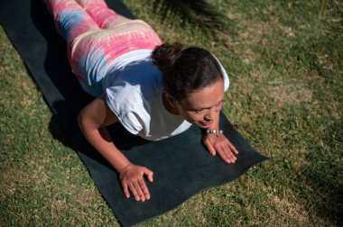 Kobra pozuyla yoga yapan bir kadının parktaki bir paspasın üzerinde görüntüsü. Yoga yapmak farkındalığı, barışı ve fiziksel sağlığı teşvik eder..