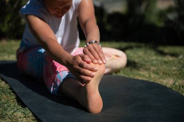 Yoga minderinin üzerinde uzanan bir kadının yakın çekimi. O, ayağını ve bacağını esnetmeye odaklandı. Ayar güneşli bir gün, rahatlama ve zindeliği teşvik ediyor..