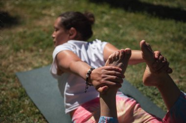 Dışarıda yoga yapan bir kadın, parkta bir paspasın üzerinde geriniyor. Görüntü zindelik, rahatlama ve doğayla olan bağın özünü yakalar..