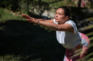 Bir kadın açık havada yoga pozu veriyor, güneşli ve doğal ortamda rahatlama, denge ve farkındalık vurguluyor..