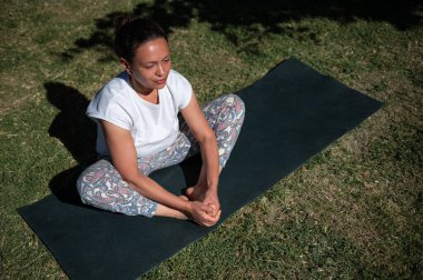 Güneşli bir günde, sakin bir meditasyon pozuyla yoga yapan bir kadın, doğal ortamdaki rahatlama ve farkındalığı teşvik ediyor..