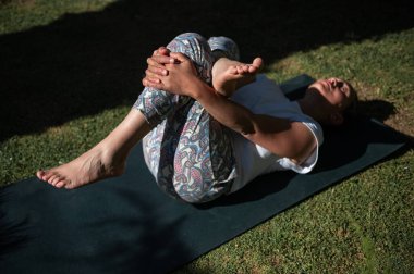 Dışarıdaki minderde yoga egzersizi yapan bir kadın. Görüntü onu güneş ışığı altında rahat ve odaklanmış bir şekilde yakalıyor..