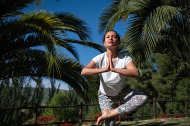 Ağaçtaki kadın dışarıda, tropikal bir ortamda yoga yapıyor. Sakin ve sakin atmosfer rahatlamayı, dengeyi ve farkındalığı teşvik eder..