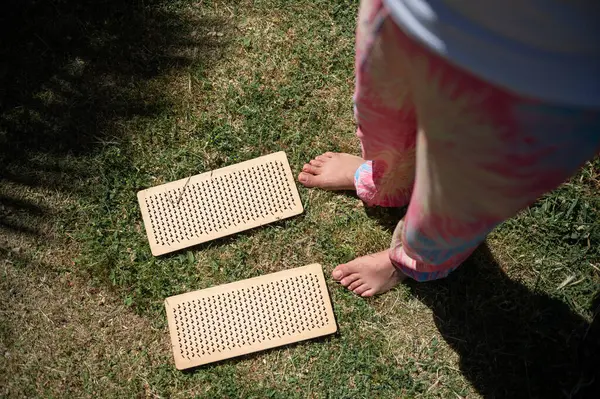 stock image A woman standing on grass with wooden foot massage mats. The image conveys relaxation and health benefits through natural foot massage techniques in an outdoor setting.