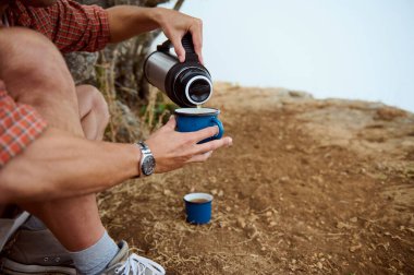 Sıcak içeceği termostan açık havada mavi bir bardağa döken birinin yakın çekimi. Rahatlama, macera ve doğa kavramları.