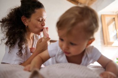 Bir annenin bebeğinin ayağını öptüğü hassas bir an onlar yatakta oynarken sevgi, ilgi ve aile bağlarını sergilerken sıcacık bir evde.