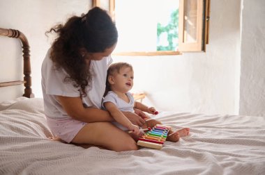 Anne ve bebek rahat bir yatakta ksilofon çalarken hassas bir anı paylaşıyorlar. Oda doğal güneş ışığıyla dolu. Aralarındaki bağın altını çiziyor ve sıcak bir atmosfer yaratıyor..