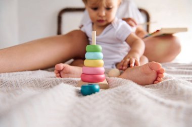 Sevimli çocuk evdeki yatağın üzerinde renkli bir oyuncakla oynuyor. Samimi bir ortamda çocuk gelişimi, eğitim ve ebeveyn-çocuk bağlarını gösteren mükemmel bir resim.