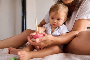 Bir anne ve bebeği evde tahta bir oyuncakla meşgul oluyor. Görüntü, bir çocuğun sıcaklığını, bağlanmasını ve erken gelişim evrelerini yakalar..