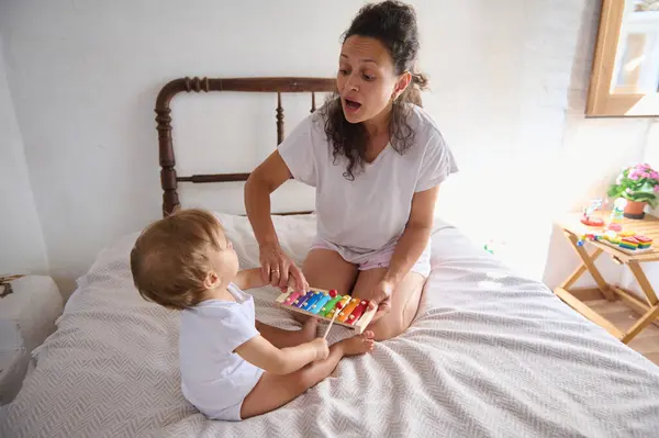 stock image Mother and baby enjoying quality time playing a colorful xylophone together in a cozy bedroom setting. The scene captures bonding, family love, and early childhood development.