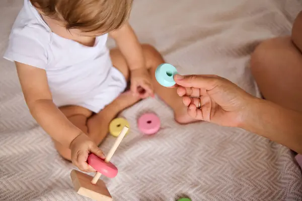 stock image A close-up shot of a baby engaging with a colorful stacking toy while a parent offers guidance and support. Perfect for themes of early learning, parent-child bonding, and developmental play.