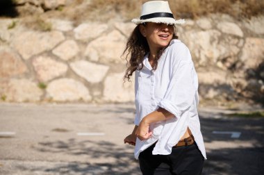 Neşeli bir kadın güneşli bir günde dışarıda vakit geçirirken mutluluğunu ifade ediyor. Öylesine giyinmiş ve şık bir şapka takıyor..