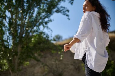 Güneşli bir günde açık havada dolaşan beyaz tişörtlü bir kadın. Sahne, doğa tarafından çevrelenmiş bir özgürlük ve rahatlama duygusunu yakalar..