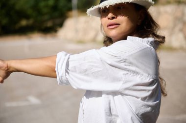 Beyaz gömlekli ve şapkalı kendinden emin kadın güneşli bir ortamda amacı olan, yönü vurgulayan ve odaklanan..