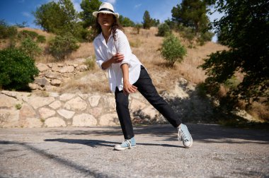 Güneşli bir günde beyaz gömlek giyen ve şapka takan bir kadın özgürlüğünü ve neşesini sergiliyor. Gündelik ve kaygısız.