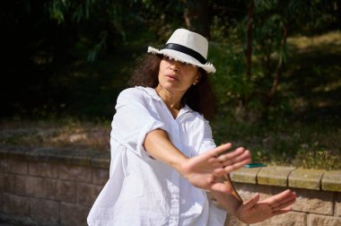 Beyaz gömlekli, şapkalı, kendine güveni tam bir kadın. Elleriyle blok yapıyor. Açık havanın tadını çıkarıyor..