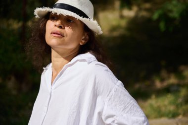 Beyaz gömlek ve şapka giyen bir kadın güneşli bir günde açık havanın keyfini çıkararak rahatlama ve yansıma yayar. Yaşam tarzı ya da doğa temalı kavramlar için mükemmel.